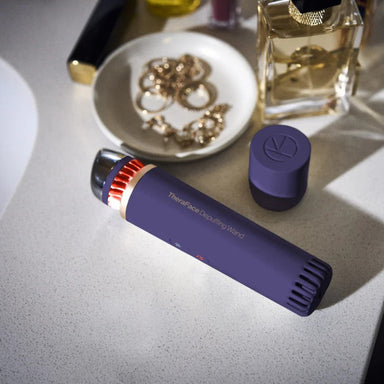 Purple hair styling tool on a surface with jewelry and perfume in the background