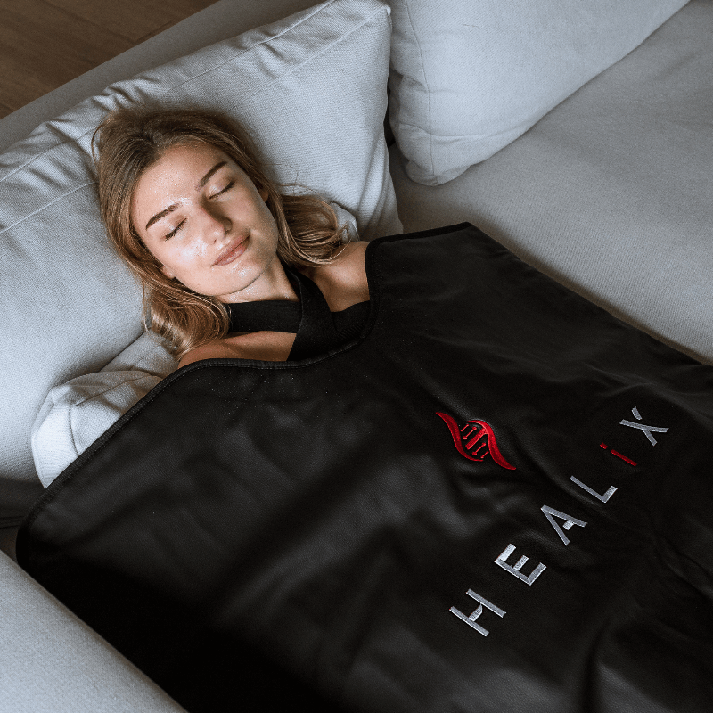 Woman lying on a couch with a black HEALIX blanket draped over her
