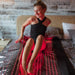 Woman sitting on a bed with red light draped over her, in a room with wooden walls.
