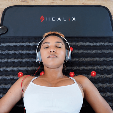 Woman lying on a HEALIX mat with headphones on, surrounded by red lights.