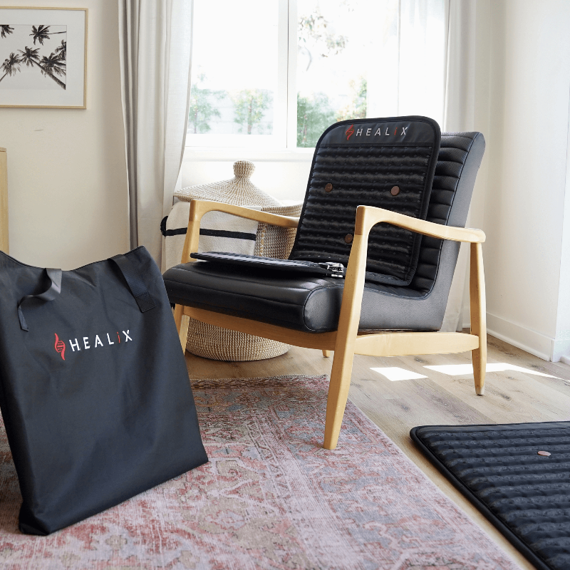 Black HEALX chair and carrying bag in a room with a window and rug.
