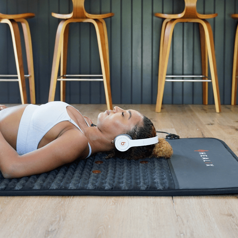 Person lying on a pemf mat with headphones on, surrounded by wooden stools.