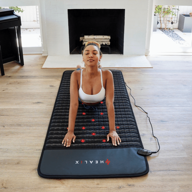 Woman using a black massage mat with red nodes in a living room.
