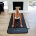 Woman using a black massage mat with red nodes in a living room.