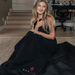Woman wrapped in a black sauna blanket with a visible brand logo in a home setting