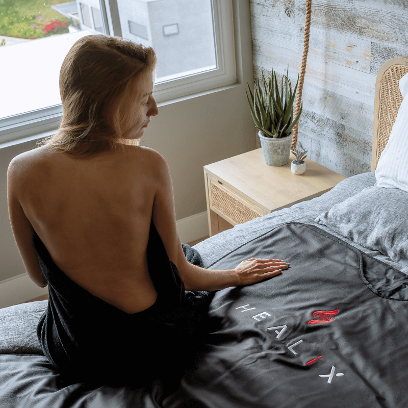 Woman sitting on a bed with a 'HEALIX' blanket in a bedroom setting.
