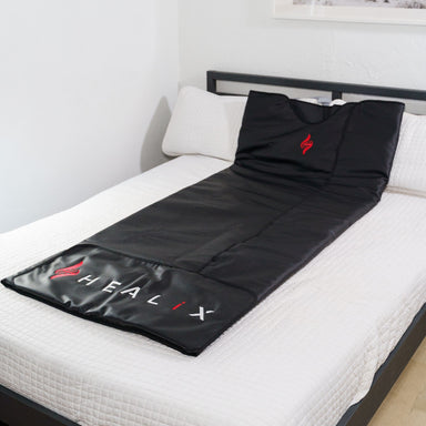 Black sauna mat with 'HALX' branding on a white bed