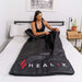 Woman using a black HEALiX sauna blanket on a bed