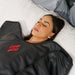 Woman lying down with a black sauna blanket featuring a red logo on a white surface.