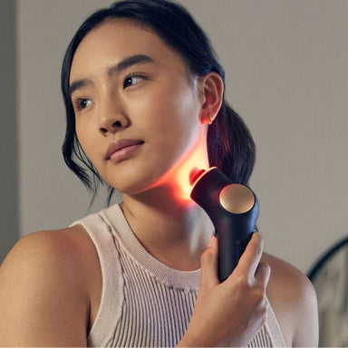 Woman using a handheld device on her neck with a neutral background