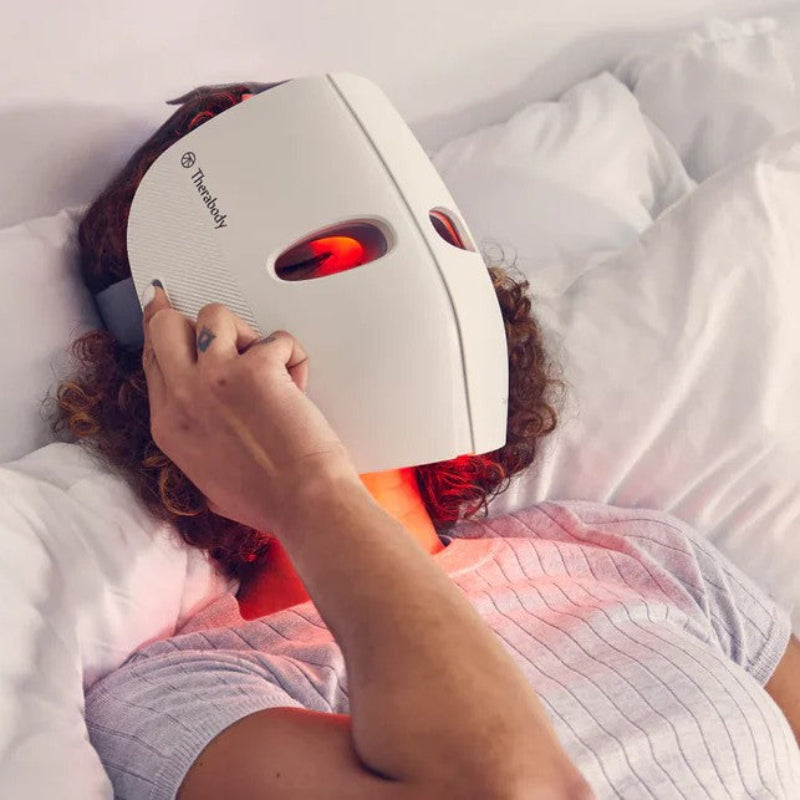 Person using a white LED face mask with red light on a white background