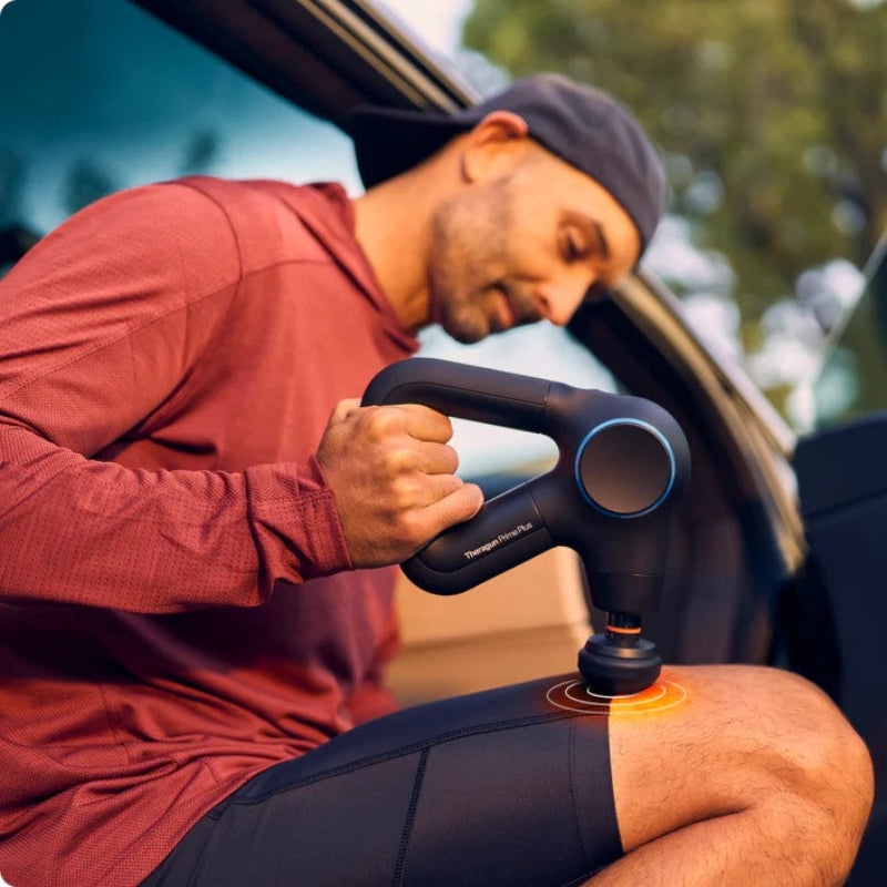 Man using a massage gun on his leg while sitting in a car