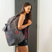 Woman carrying a gray backpack with a visible brand logo, standing indoors.