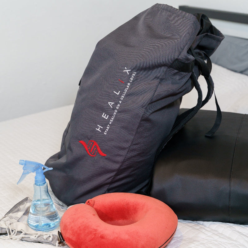 Black travel bag with HEALIX branding on a bed next to a red neck pillow and spray bottle.