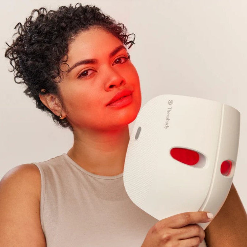 Woman holding a white device with red lights on a plain background