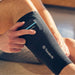 Person wearing a Therabody compression sock with a device attached, sitting on a couch.
