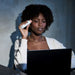 Woman holding a white object near her ear, using a laptop with a dark background
