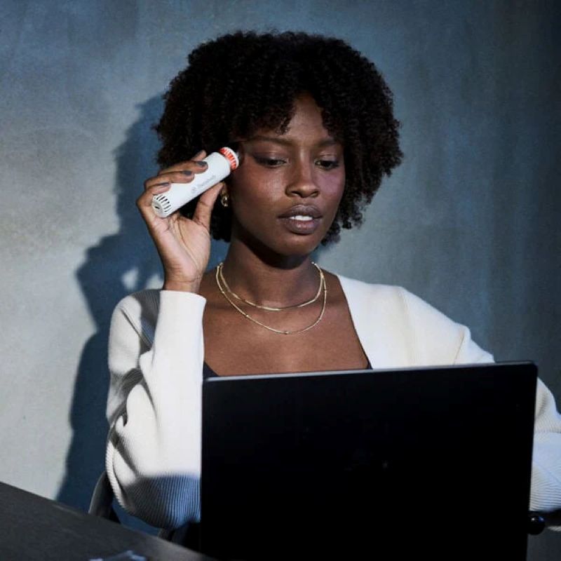 Woman holding a white object near her ear, using a laptop with a dark background