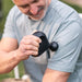 Man using a black handheld device, possibly for health or fitness purposes, outdoors.